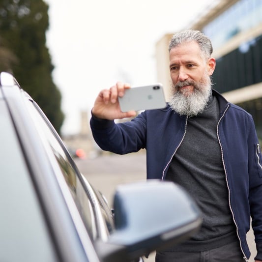 Man taking pictures of the car Ein Mann macht Fotos von seinem Auto mit dem Smartphone
