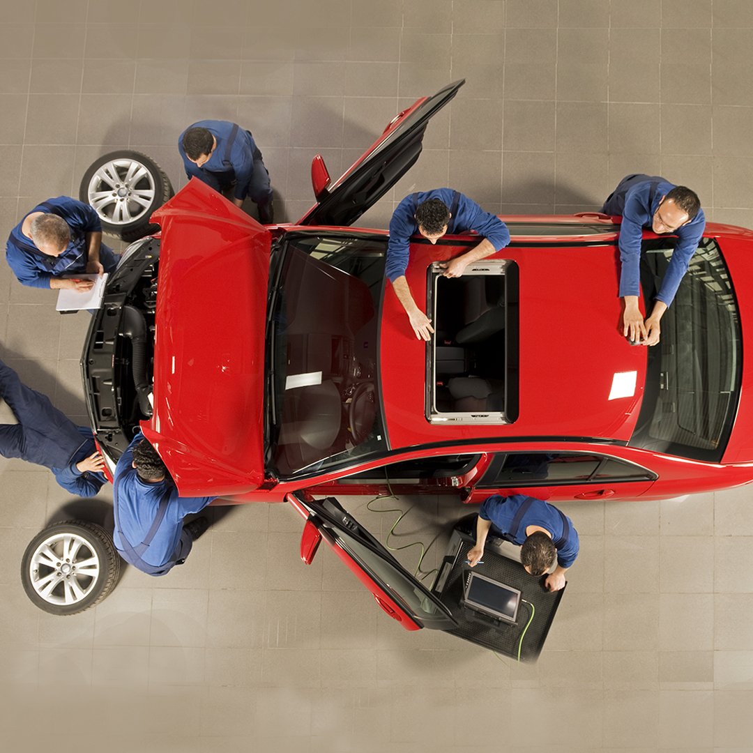 Rotes Auto wird von mehreren Mechanikern in der Werkstatt repariert