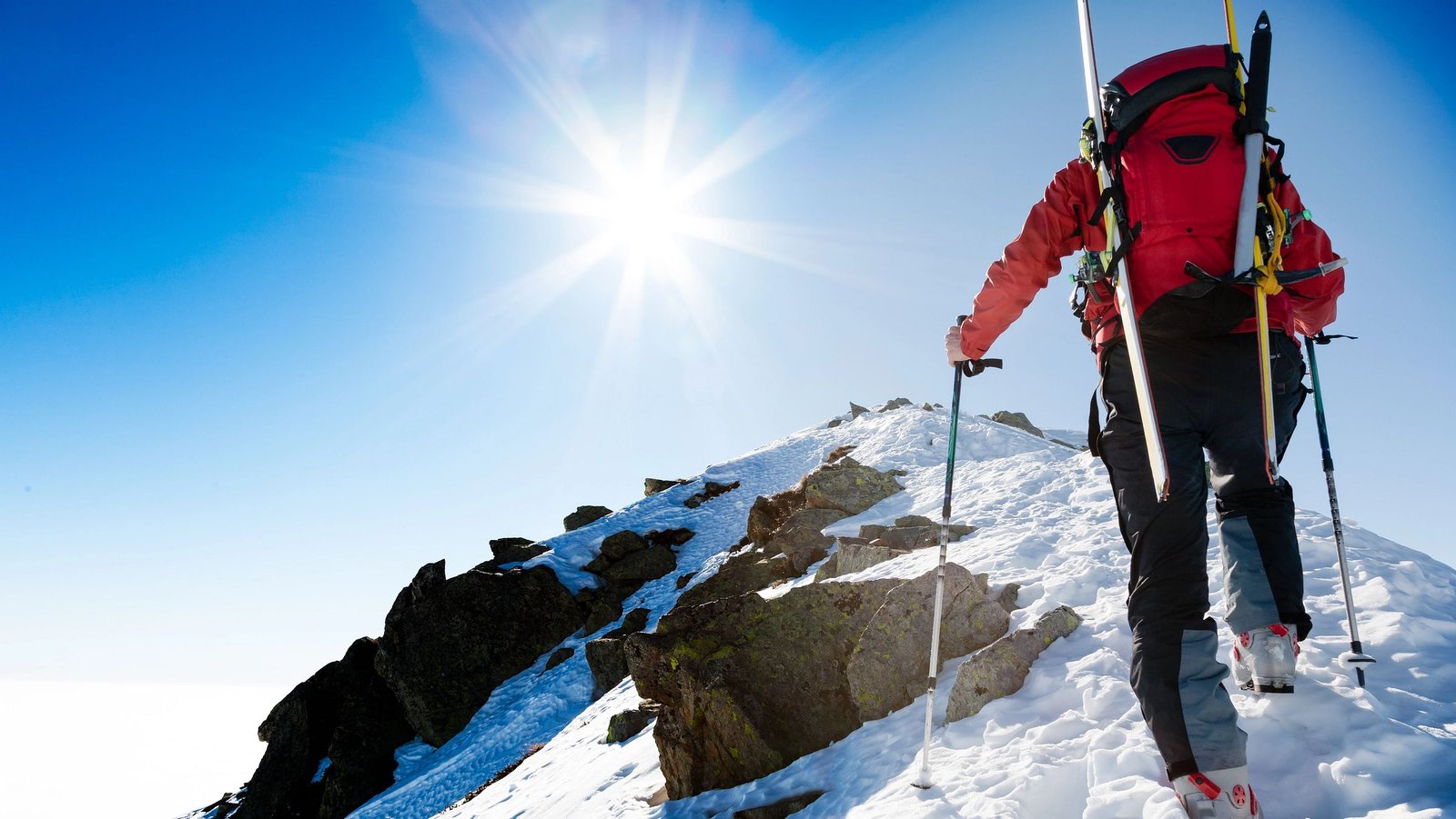 Mann steigt mit Tourenski auf den Gipfel.