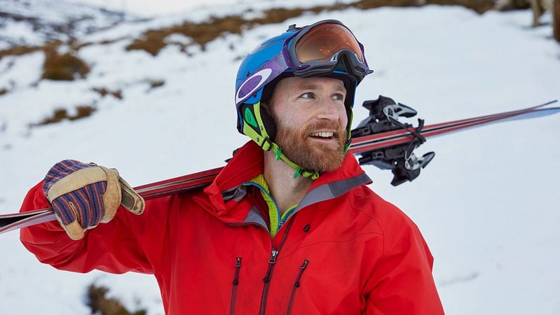 Mann mit roter Jacke trägt Ski auf der Schulter