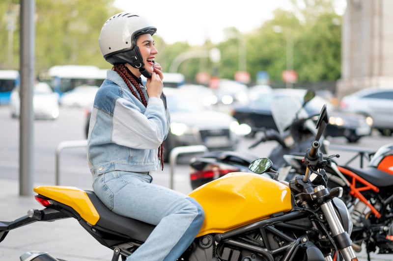 Dame sitzt am Motorrad und macht den Helm zu