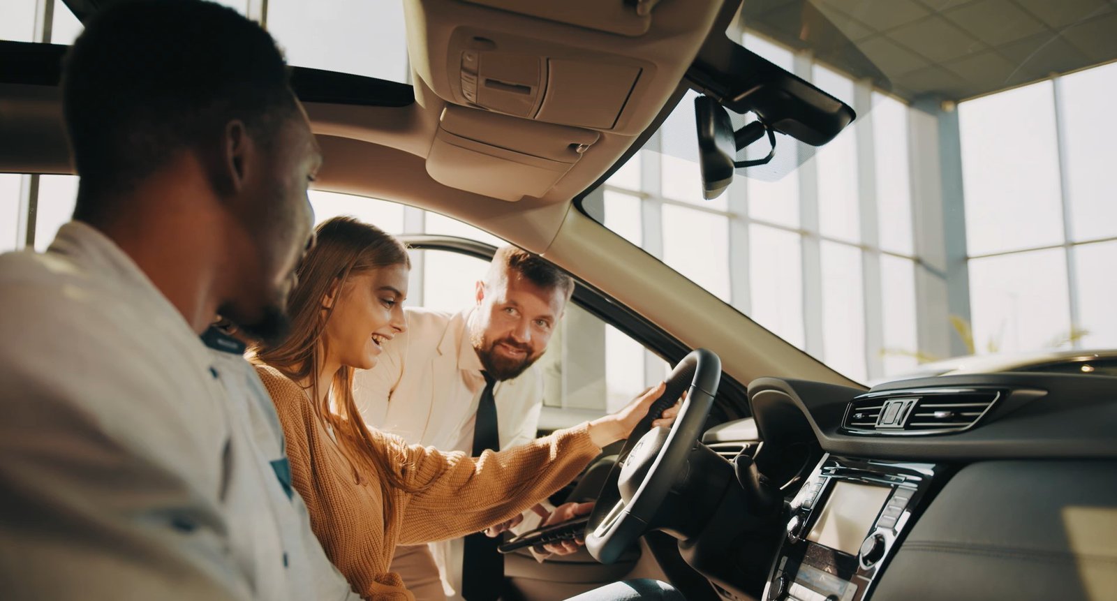 Ein Pärchen sitzt in einem Neuwagen, Verkäufer schaut in das Auto