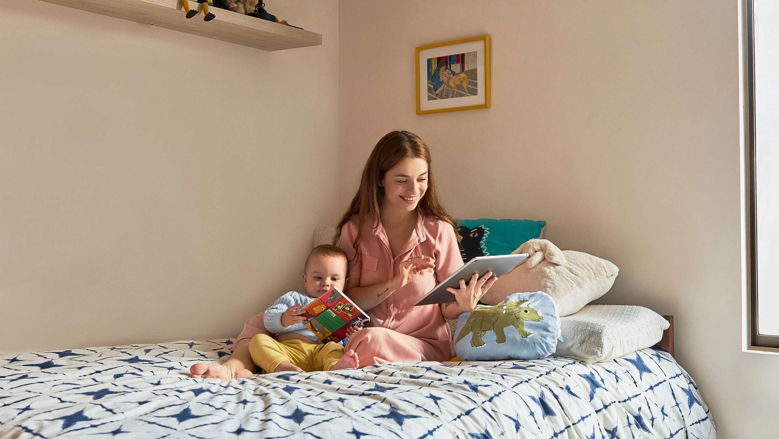 Mutter sitzt lachend im Bett und liest einem Kleinkind eine Geschichte vor.