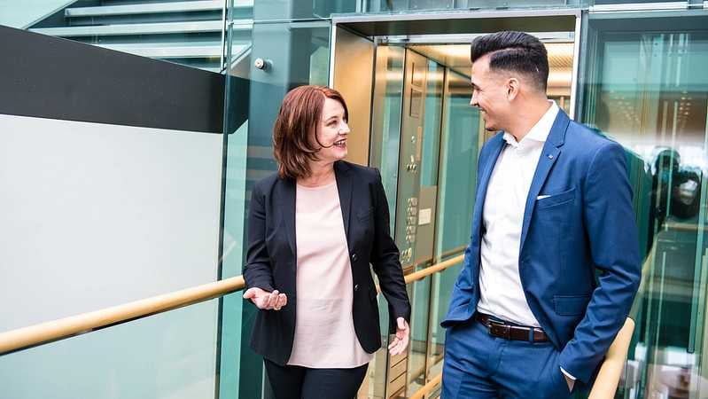 Zwei Kundenberater gehen am Gang und unterhalten sich lachend.