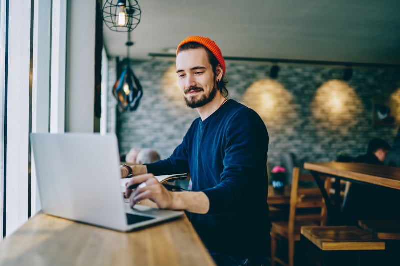 Ein Mann sitzt entspannt vor dem Laptop und arbeitet in einem Cafe.