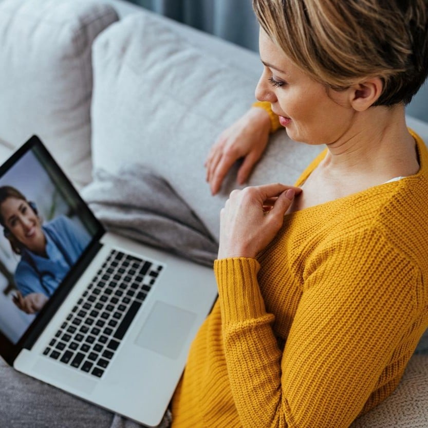 Dame sitzt auf der Couch und telefoniert über den Laptop mit der Wohn-Assistance von Zurich