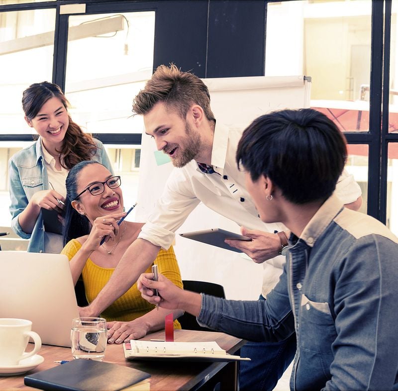 Mitarbeitende sitzen oder stehen lachend vor dem Firmenlaptop
