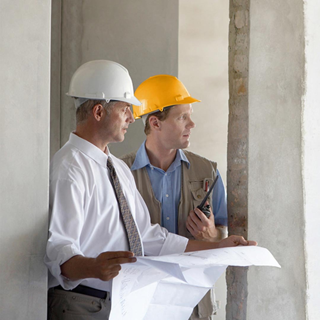 Zwei Männer mit Helmen stehen mit einem Plan in der Hand auf einer Baustelle