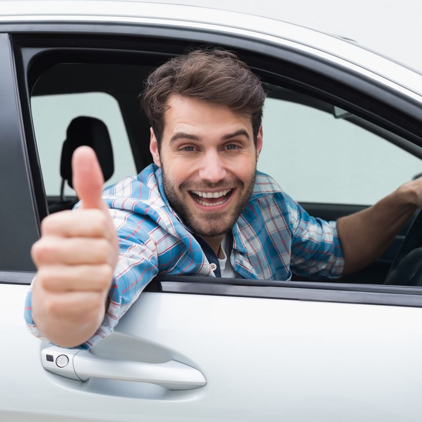 Mann sitzt im Auto und zeigt mit dem Daumen hoch