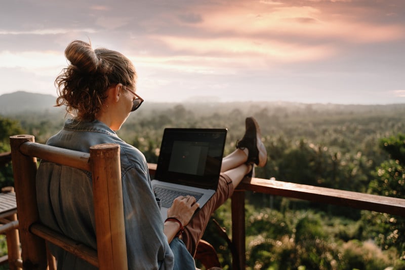Junge Frau am Laptop auf Terrasse mit atemberaubender Aussicht in die Natur