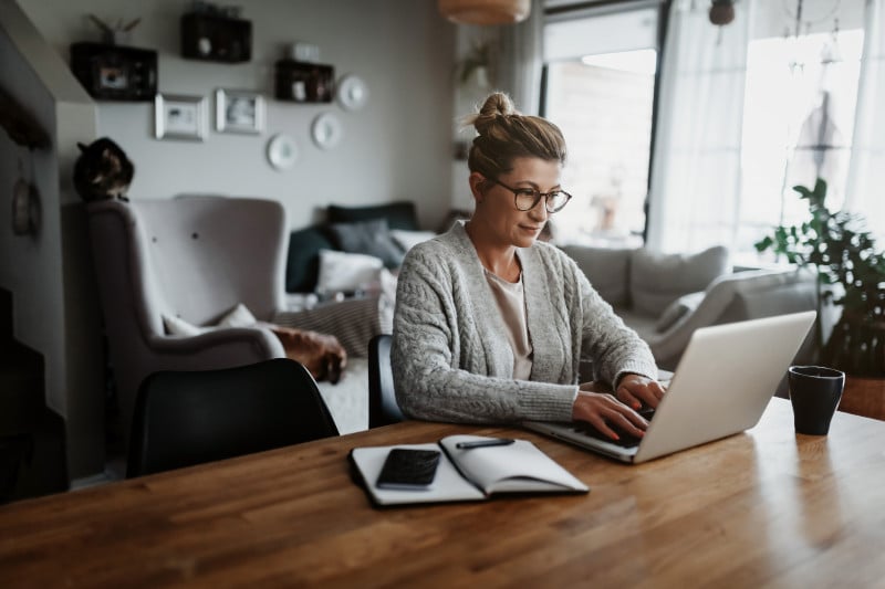 Frau mit Brille sitzt zuhause am Esstisch und arbeitet am Laptop